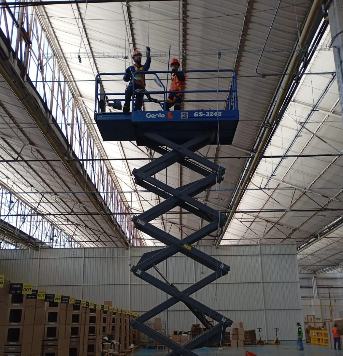 Tijera extendida con dos operadores bajo la cubierta de una nave industrial