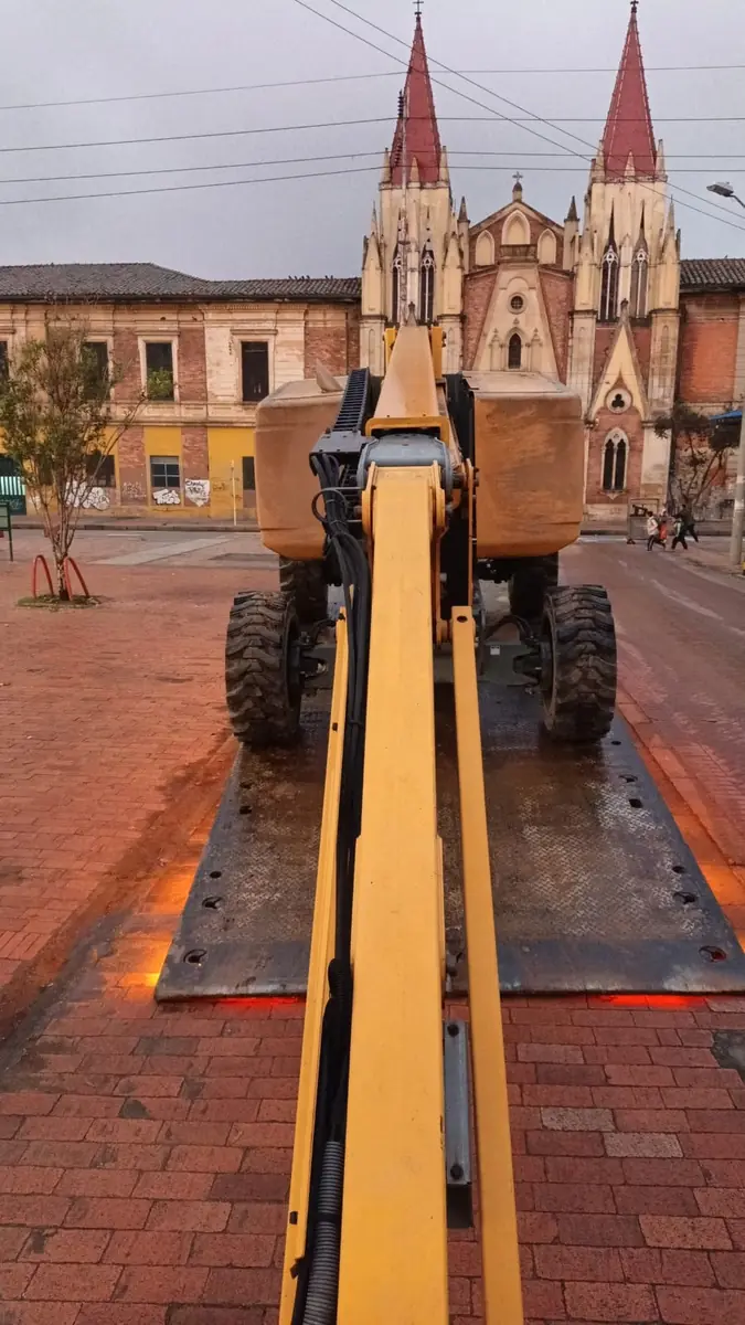 Manlift asegurado sobre la plataforma de una grúa planchón frente a una iglesia